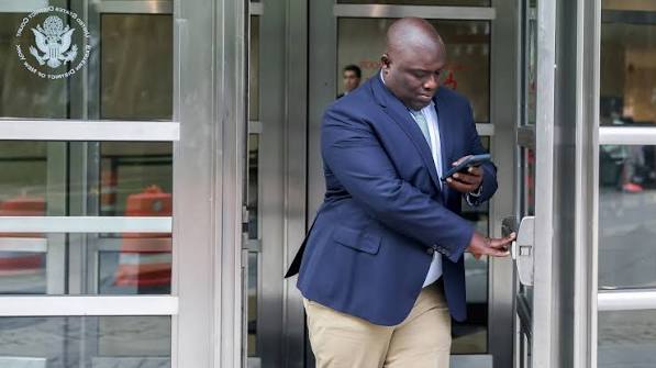 Former-Goldman-Sachs-investment-banker-convicted-of-foreign-bribery-money-laundering | Ghanaguardian.com Man in a blue blazer and beige pants opens glass doors while looking at his phone; DHS seal visible in the upper left corner.