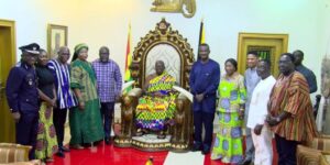 Group of officials and guests posing around a seated leader on an ornate throne in a ceremonial room, flags in view.