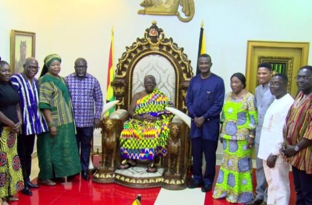 Group of officials and guests posing around a seated leader on an ornate throne in a ceremonial room, flags in view.