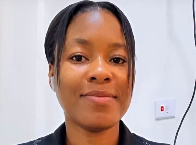 Close-up portrait of a woman with straight black hair, looking at the camera, in a light-colored room.