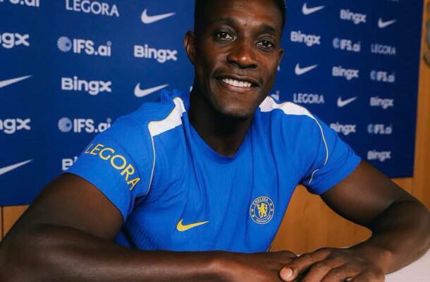 Chelsea FC player in a blue kit sits at a press conference, smiling, with a sponsor backdrop and 'Presented by LEGORA' text.