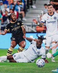 Soccer players collide for the ball on a green field: two Inter Milan players in white kits, one sliding, while a Manchester City player in black presses nearby.