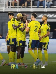 Yellow-clad soccer players celebrate on the field after a final 2-2 draw. The scoreline and team crests are shown at the bottom.