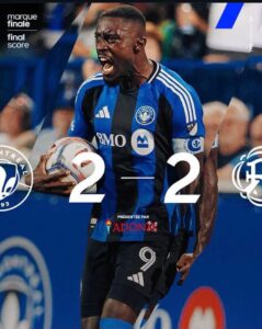 Soccer player in a blue and black kit celebrating with a ball as a 2–2 final score graphic is overlaid, with team logos and sponsor text nearby.