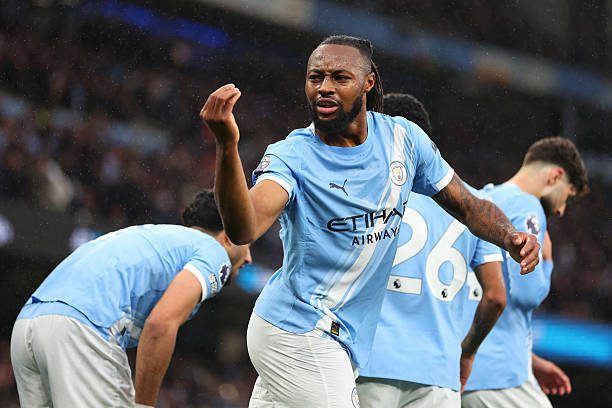 Manchester City players celebrate on the field, front and center player raises a fist in triumph.