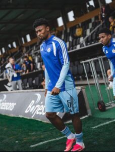 Soccer player in a blue training kit with number 5 walking along the sideline near the dugout.