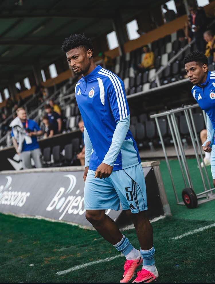 Soccer player in a blue training kit with number 5 walking along the sideline near the dugout.