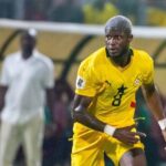 Soccer player in a yellow kit with number 8 dribbling on the field during a match, bench area in the background