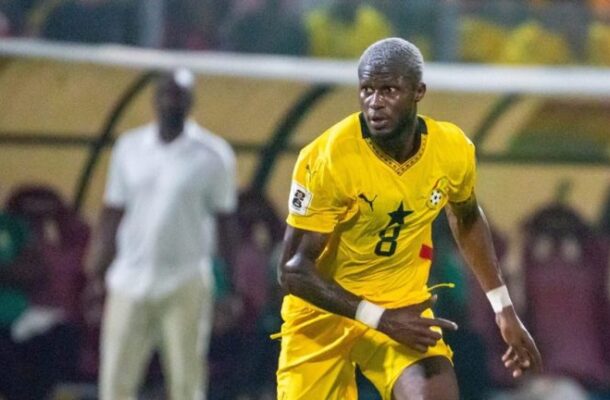 Soccer player in a yellow kit with number 8 dribbling on the field during a match, bench area in the background