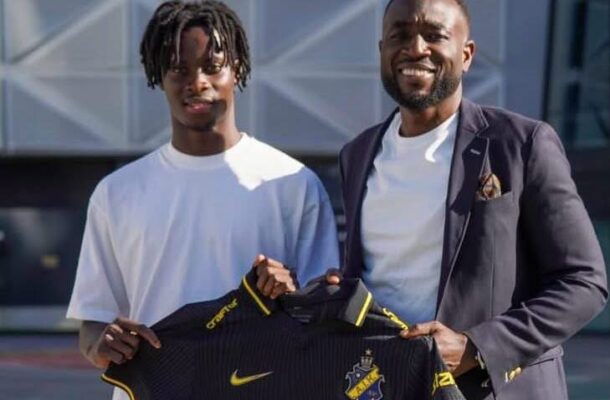 IMG_1561 | Ghanaguardian.com Two men stand outside a modern building, holding up a black soccer jersey with yellow trim and the sponsor 'truecaller'.