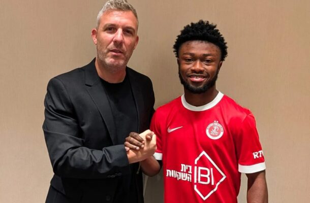 IMG_1562 | Ghanaguardian.com Two men shake hands and smile for the camera; one in a black blazer, the other in a red sports jersey, against a beige wall background.
