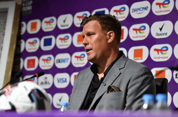 IMG_1564 | Ghanaguardian.com Man in gray suit speaking at a press conference, purple backdrop with sponsor logos behind him.
