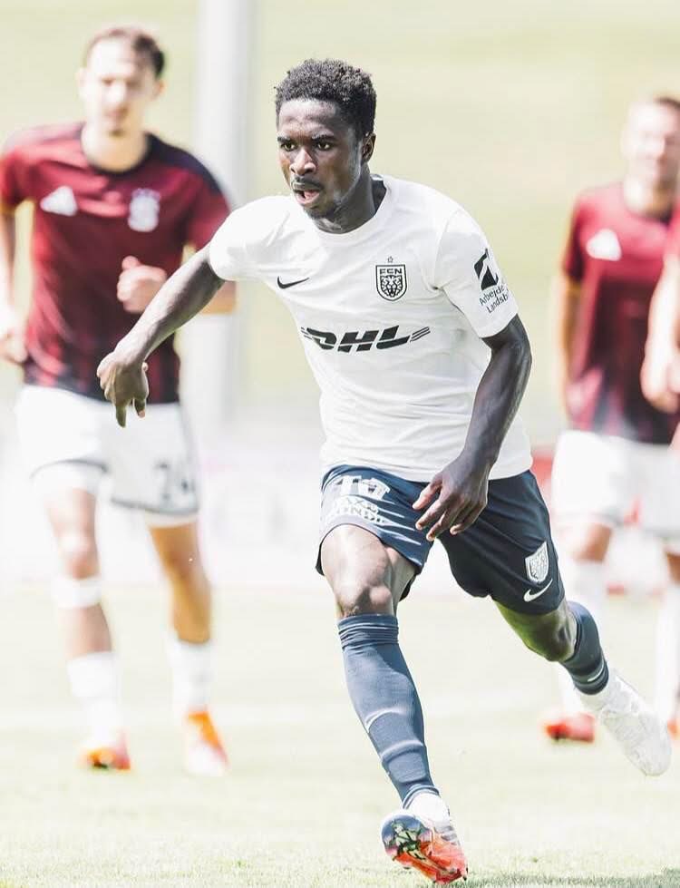 Soccer player in a white jersey dribbles the ball while sprinting downfield during a match, defenders in maroon behind him.