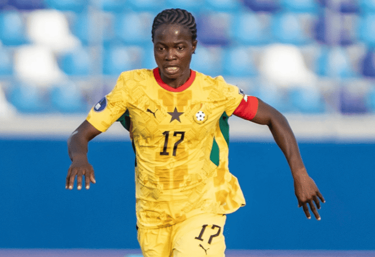 Female footballer in a yellow kit with number 17 running on the field during a match, arms out for balance, in a blue stadium background.