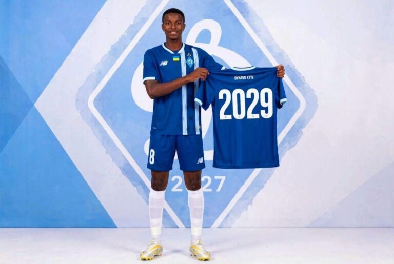 Male footballer in a blue Dynamo Kyiv kit holds up a matching jersey with the number 2029 against a blue geometric backdrop.