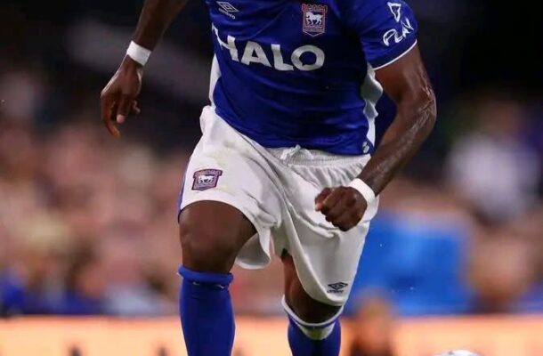 Soccer player in a blue kit sprinting with the ball on a green pitch, pink cleats and white shorts, focused on the move.