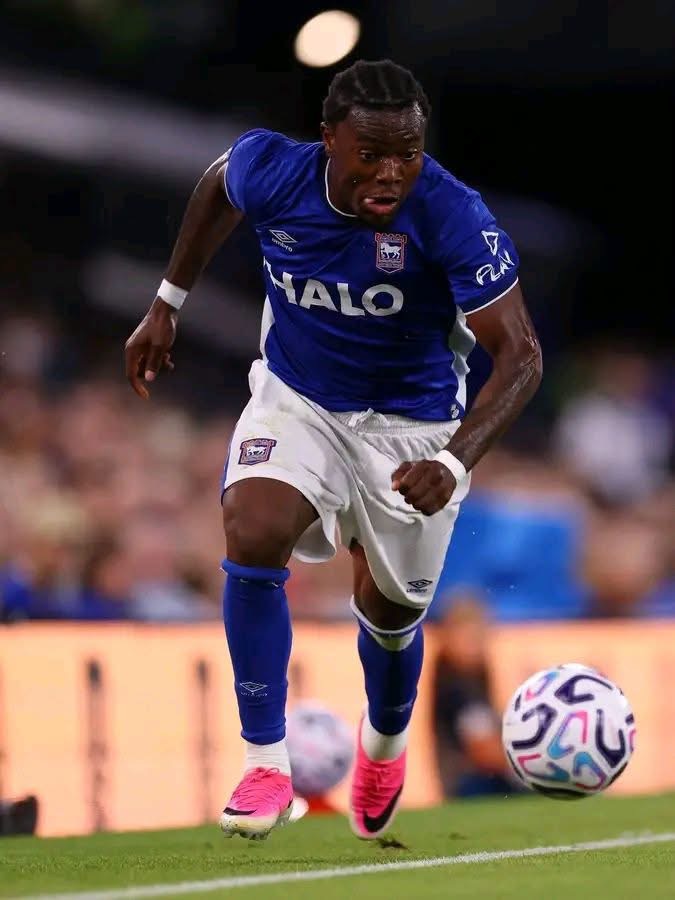 Soccer player in a blue kit sprinting with the ball on a green pitch, pink cleats and white shorts, focused on the move.