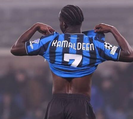 Soccer player lifting a blue-and-black striped jersey to reveal the back with name Ramaldeen and number 7, arms raised in a stadium