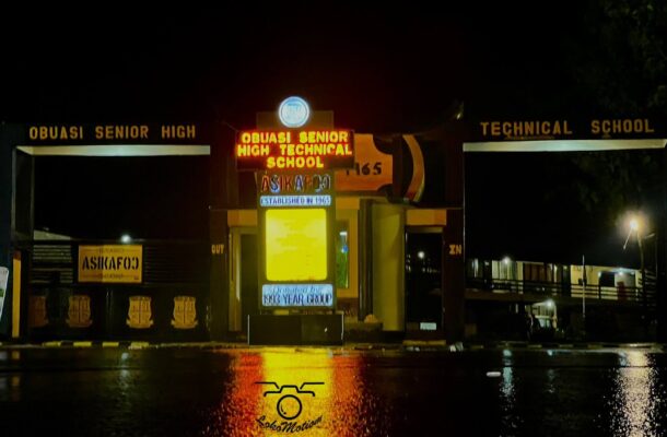 Night view of Obuasi Senior High Technical School entrance with illuminated red-and-yellow sign at night.