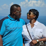 Couple wearing sunglasses gazing at each other against a sunny ocean backdrop.