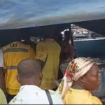 Crowd under a blue canopy at a market stall, with people wearing high‑visibility vests and casual clothing in line.