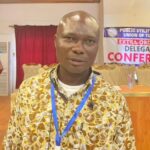 Man with a blue lanyard at a delegates conference, backdrop shows a banner for the Public Utility Workers' Union of Ghana (PUWU).