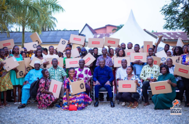 Group of people posing with Lenovo boxes at an outdoor charity event, smiling in front of a white tent.