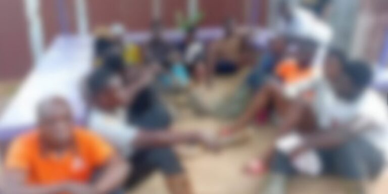 Group of people sitting in a circle outdoors, hands joined in the center.