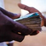 Close-up of two hands exchanging a thick stack of banknotes, with the focus on the money being handed over.