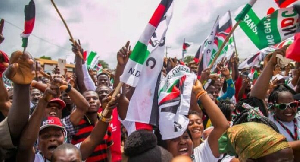 Large crowd at a political rally, waving green, white, and red flags and banners.