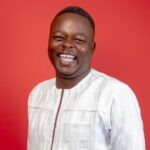 Portrait of a smiling man wearing a white traditional shirt against a red background down to the shoulders.