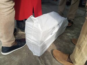 White fabric-wrapped bag on a concrete surface with several people standing nearby, visible legs and shoes around it.