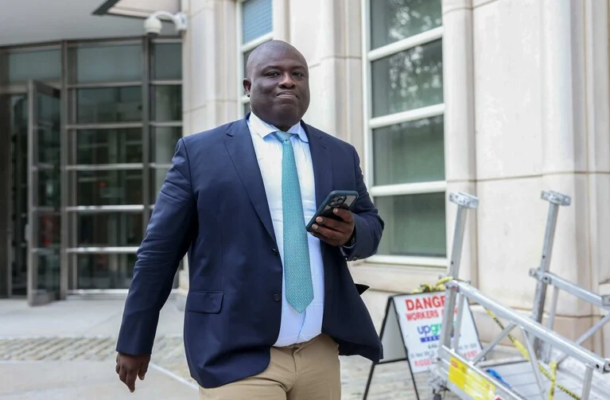 no_translation_11641_e0cy2fufqun7bgm01pwyz9lm_no_translation_translation | Ghanaguardian.com Professional man in navy suit and turquoise tie walking outside a modern building while looking at his phone.
