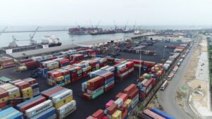 Aerial view of a busy shipping port with colorful stacked shipping containers, cranes, and ships docked at the harbor.