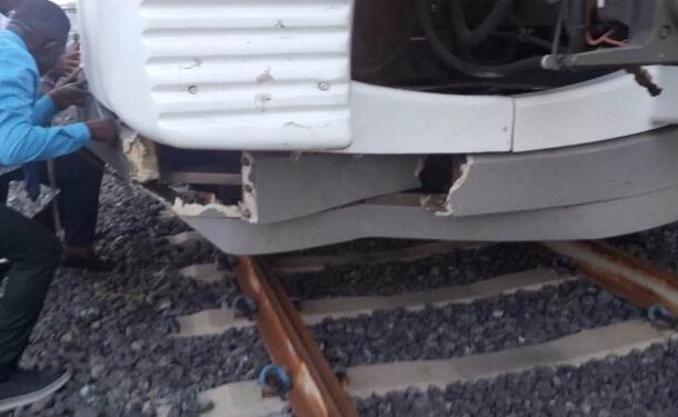 no_translation_6765_e0cy2fufqun7bgm01pwyz9lm_no_translation_translation | Ghanaguardian.com Two people crouch beside a white vehicle with a damaged front bumper wedged on railroad tracks, inspecting the damage.