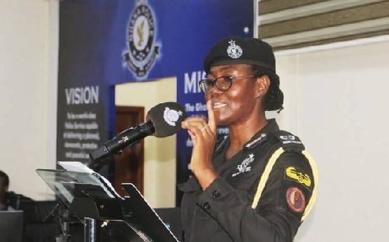 no_translation_6907_e0cy2fufqun7bgm01pwyz9lm_no_translation_translation | Ghanaguardian.com Female police officer in uniform speaks at a podium with a microphone, in front of a blue backdrop and banner.