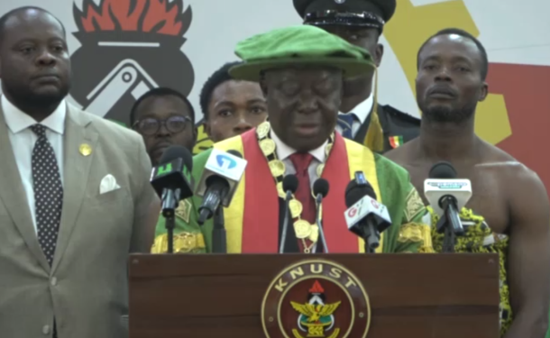 no_translation_7151_e0cy2fufqun7bgm01pwyz9lm_no_translation_translation | Ghanaguardian.com Central figure in a green hat and multicolored ceremonial sash delivering a speech at a KNUST podium, flanked by aides and reporters behind him.