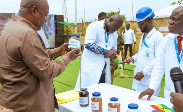 no_translation_7152_e0cy2fufqun7bgm01pwyz9lm_no_translation_translation | Ghanaguardian.com Outdoor demonstration of handwashing products: a man in a brown shirt shows a jar to presenters in white lab coats at a table with several labeled bottles, a microphone nearby.