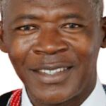Portrait of a smiling Black man wearing a white shirt and colorful patterned vest against a white background to convey friendliness and cultural dress.