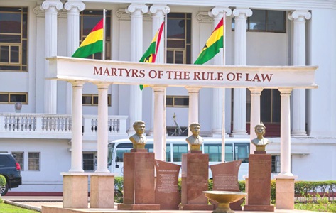 no_translation_7525_e0cy2fufqun7bgm01pwyz9lm_no_translation_translation | Ghanaguardian.com Busts on stone pedestals in front of a columned building; banner reads 'MARTYRS OF THE RULE OF LAW' with three flags overhead.
