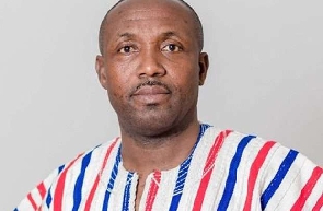 Portrait of a man facing the camera in a blue, red, and white striped traditional shirt against a light gray background.