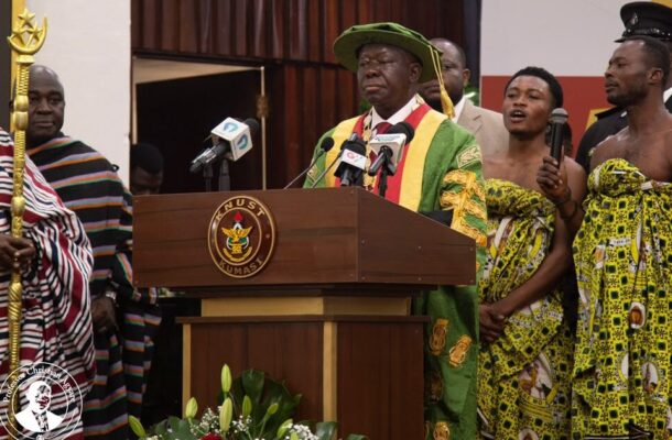 no_translation_7569_e0cy2fufqun7bgm01pwyz9lm_no_translation_translation | Ghanaguardian.com Man in green and gold ceremonial robes speaks at a wooden podium with microphones, KNUST Kumasi insignia visible on the front.