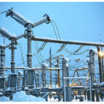 High-voltage electrical substation with transformers, insulators, and power lines in a snowy outdoor setting.