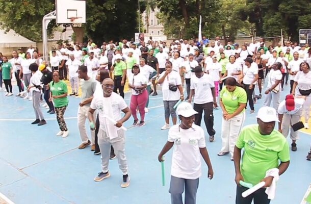 Large crowd participating in an outdoor group exercise on a blue basketball court, mostly in white shirts with some green outfits.