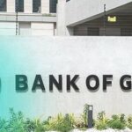 Exterior wall with the large 'BANK OF GHANA' sign and a green circular Bank of Ghana seal on the left, plus landscaped plants in front.