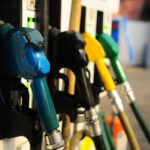 Diesel fuel pump nozzles at a gas station, blue nozzle in focus with other colored hoses in the background (fuel pumps).