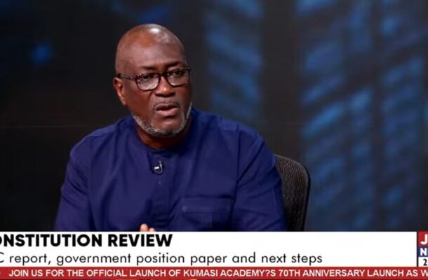 no_translation_8622_e0cy2fufqun7bgm01pwyz9lm_no_translation_translation | Ghanaguardian.com Man in a blue shirt wearing glasses speaks in a TV studio about constitution review, with a microphone clipped to his shirt and Joy News branding visible.